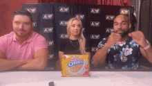 three people sitting in front of a wall with aew written on it