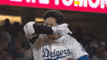 a baseball player wearing a dodgers jersey is covering his face with his glove .
