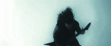 a man with long hair is playing a guitar in the dark .