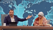 a man and a woman are sitting at a table in front of a world map