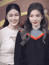 a woman wearing a prada shirt is standing next to a woman wearing a graduation gown