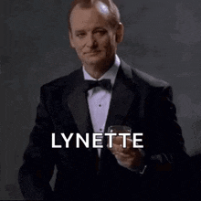 a man in a tuxedo and bow tie is holding a glass of whiskey and pointing at the camera .