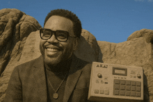 a man wearing glasses and a suit is holding a small akai device
