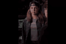 two women are standing next to each other in a dark room . one of the women is wearing a baseball cap .