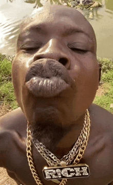 a man wearing a necklace with the word rich on it blows a kiss