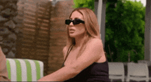 a woman wearing sunglasses and a black tank top is sitting in a chair .