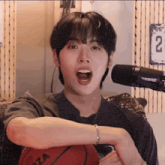 a young man holds a basketball in front of a shure microphone with the number 22 on the wall behind him