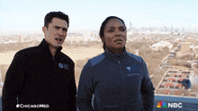 a man and a woman are standing in front of a city skyline and the nbc logo