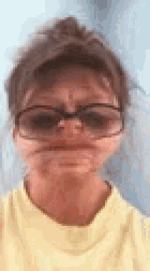 a woman wearing glasses and a yellow shirt making a funny face .