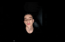 a young man in a black shirt is looking at the camera in the dark