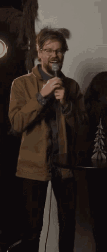 a man wearing glasses and a brown jacket is holding a microphone