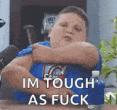 a fat boy is sitting at a table with a microphone and a bottle of water and making a funny face .