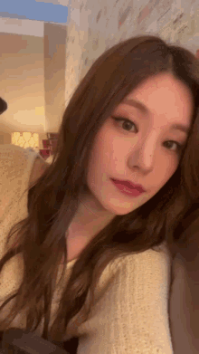 a close up of a woman taking a selfie in a room . she is wearing a white sweater .