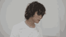 a young man with long curly hair wearing a white shirt