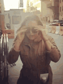 a woman wearing sunglasses is standing on a street with a bottle of water in her hand