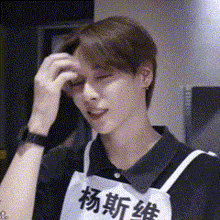 a man wearing a black shirt and an apron with chinese writing on it is scratching his head .
