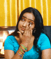 a woman in a blue shirt with bracelets on her wrists is covering her face with her hand