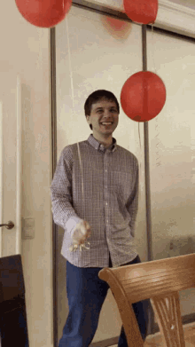 a man in a plaid shirt stands in front of a glass door with red balloons hanging from it