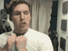 a man in a white shirt is adjusting his tie in a room .