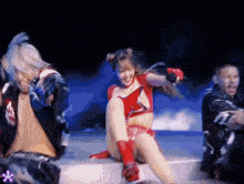 a woman in a red crop top is sitting on a stage with two men dancing behind her
