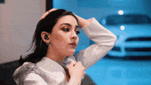 a woman in a white jacket has her hand on her hair