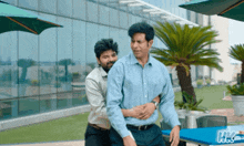 a man is hugging another man in front of a building with hk3 written on it