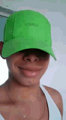 a man wearing a green hat is smiling and wearing a white tank top .