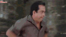 a man in a brown shirt is standing with his hands on his hips and making a funny face .