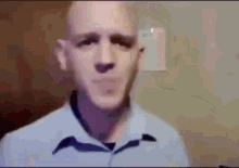 a bald man in a blue shirt is making a funny face while looking at the camera .