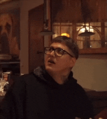 a man wearing glasses and a black hoodie is standing in a dark room .
