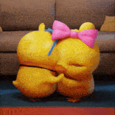 two yellow ducks with pink bows on their heads are hugging each other in front of a couch