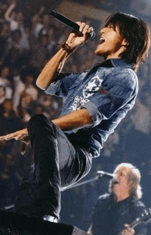 a man in a denim shirt is singing into a microphone on stage .