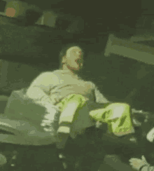 a man in a gray sweater and yellow pants is sitting on a chair with his mouth open .