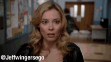 a woman with a surprised look on her face is standing in a hallway next to a sign that says jeffwingersego