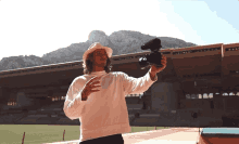 a man in a hat holds a camera in front of a stadium