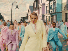 a woman in a yellow suit stands in front of a crowd of people in pink suits