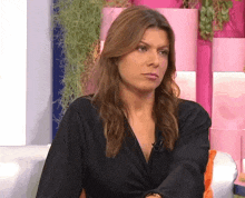 a woman in a black dress is sitting on a couch in front of a pink wall .