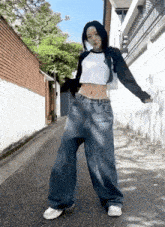 a woman wearing a crop top and wide leg jeans is standing on a street .
