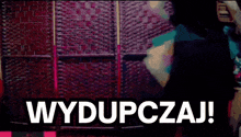 a woman is standing in front of a wall with the words wydupczaj on it
