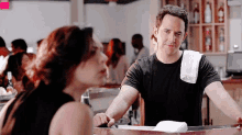a man with a towel on his shoulder is talking to a woman at a bar .