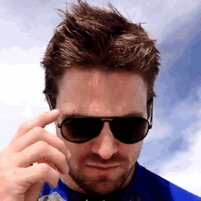 a close up of a man wearing sunglasses and a blue shirt against a blue sky