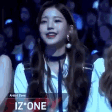 a girl with long hair is smiling in front of a crowd while wearing a choker and earrings .
