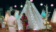 a man and woman are standing in front of a tent decorated with lights and candles