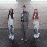 a man and two women are dancing in front of a brick wall and the man is wearing a suit and tie