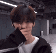 a young man is covering his mouth with his hand while standing in a room .