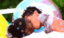 a man and woman kissing in a bathtub with bubbles surrounding them
