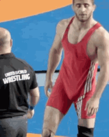 a man in a red singlet is standing next to a referee in a black shirt that says united world wrestling .