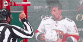 a man in a marchand jersey holds a helmet in front of a referee