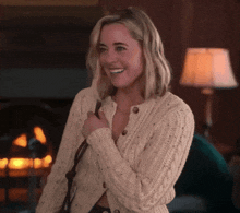 a woman in a white sweater smiles in front of a lamp
