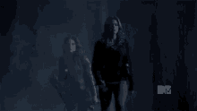 two women are walking through a dark room with a mtv logo in the corner .